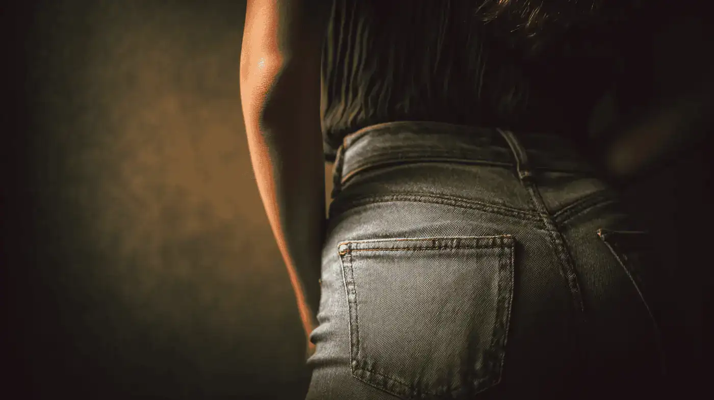 Close-up of lower back and hips of a person wearing high-waisted jeans, highlighting the buttock area relevant to buttock lift surgery discussion.