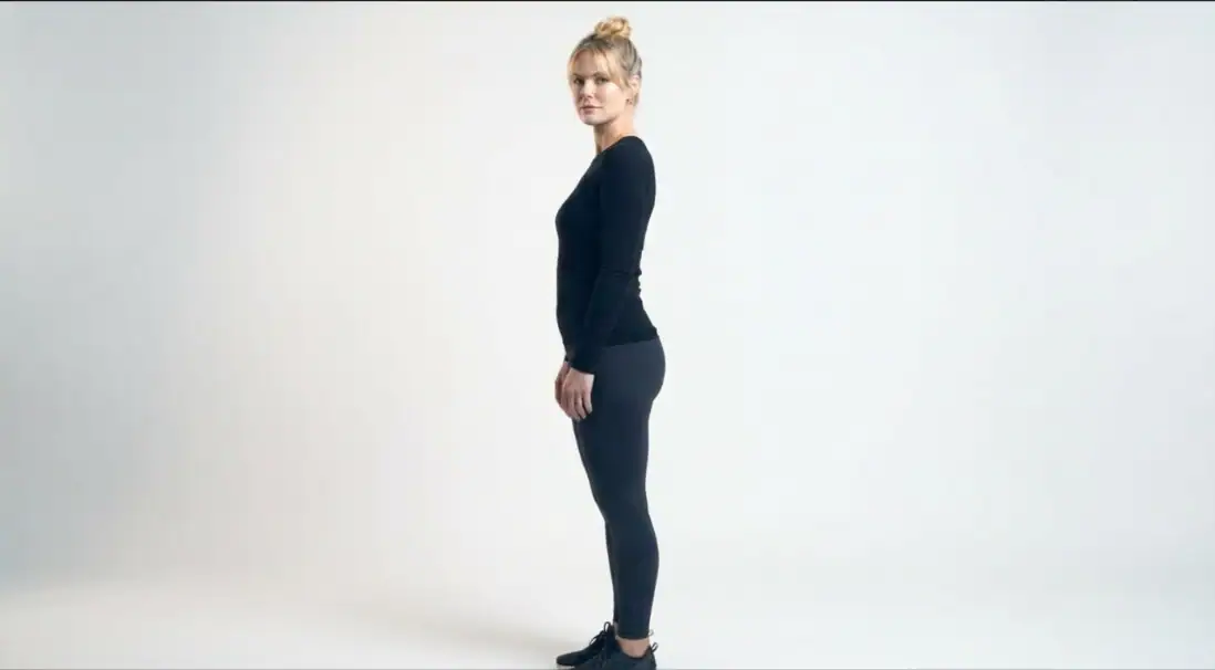 A woman standing in profile against a plain background, emphasizing a sleek and slender body shape, representing body contouring or cosmetic enhancement.